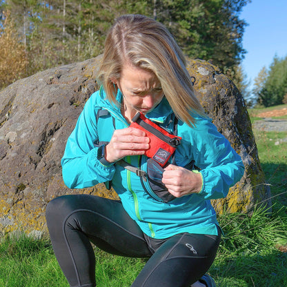 Trail runner placing Ultralight Explorer trail running and hiking first aid kit in her running vest pocket. From Cascade First Aid